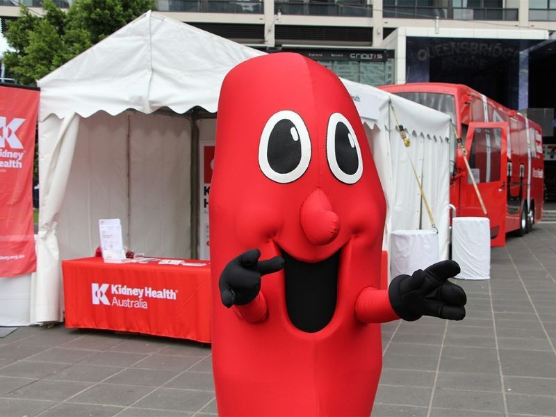 A kidney mascot stands in front of a Kidney Health Australia Big Red Bus tent