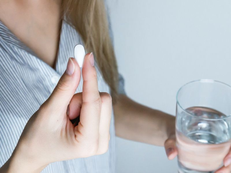 A woman holds a white pill and a glass of water