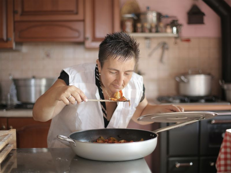 A woman tastes food from a pan