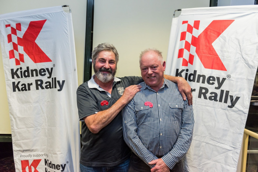 Two men posing by Kidney Kar Rally banners