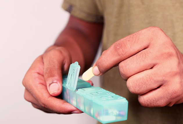 A man putting a pill capsule into a weekly pill management box