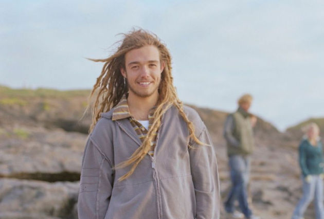 Young man standing on beach. Long hair and grey jacket