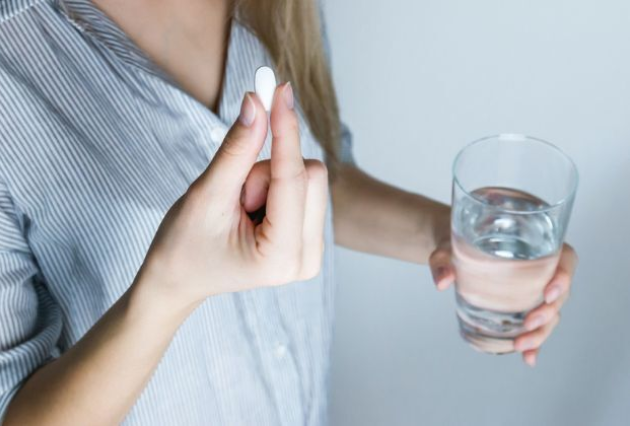 A woman holds a white pill and a glass of water