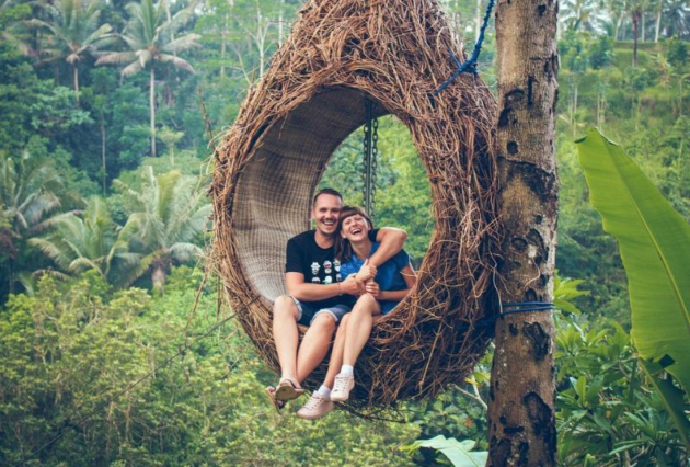 A man and woman embrace inside a hanging seat attached to a palm tree