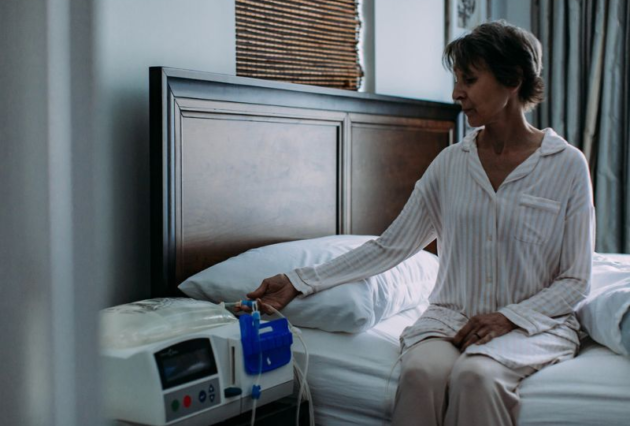 A woman sits on her bed and presses a button on her dialysis machine