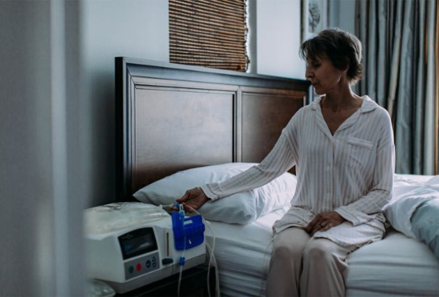 A woman sits on her bed and presses a button on her dialysis machine