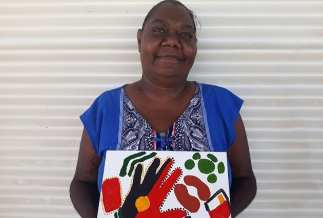 An Indigenous woman holds up her artwork
