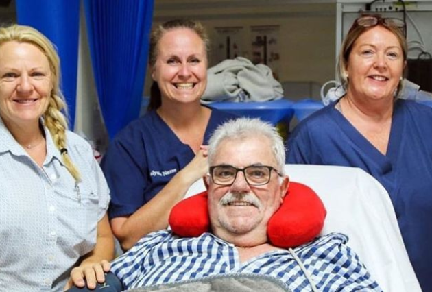 A man on dialysis poses for a photo surrounded by three female health professionals