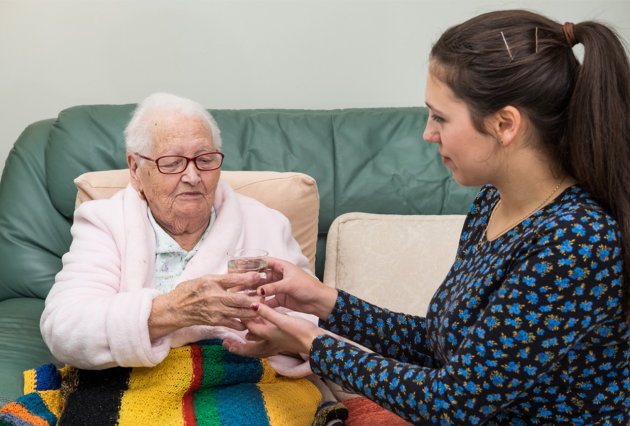 A female health professional serves a drink to an elderly woman.