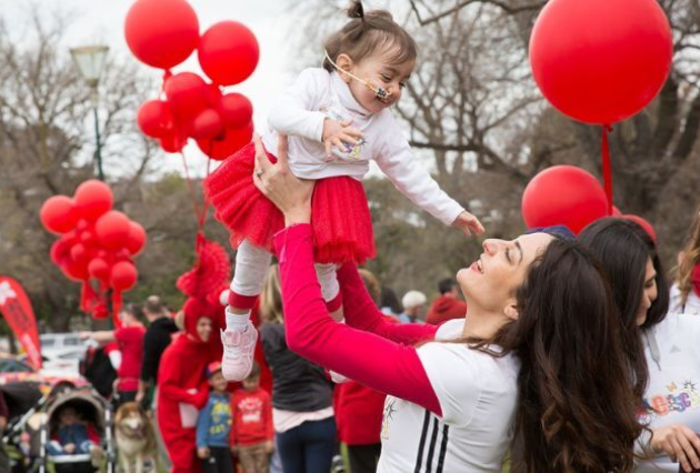 A woman holds up her baby surrounded by red balloons