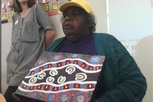 An indigenous woman holds up her art