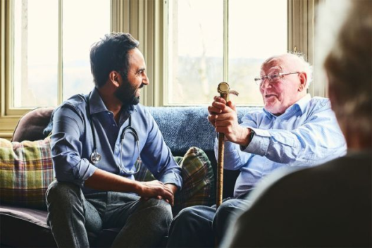 A doctor talks to an older male patient at home