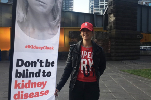 Sheree poses next to a Kidney Heath Australia banner